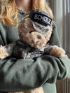 A person in a green sweater holds the Sailor Sleeptight – Navy Teddy Bear in cammo by ZZZ BEARS, complete with storybook and sleep system—ideal for any child’s nighttime routine.